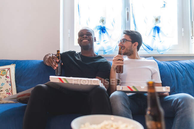 Dos hombres tomando pizza y cerveza en casa - foto de stock