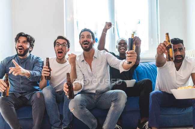 Мужчины пьют пиво и смотрят спорт по телевизору, аплодируют — стоковое фото
