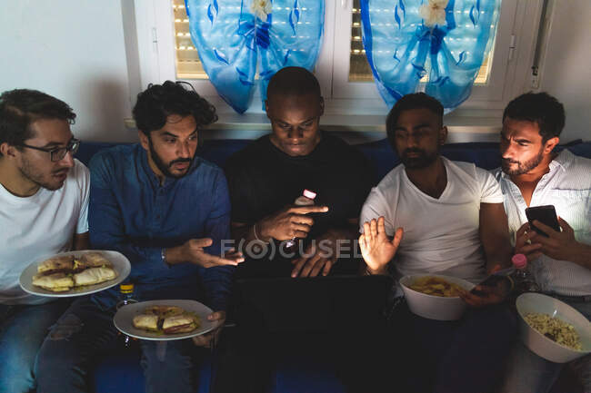 Amigos varones teniendo comida y viendo el portátil - foto de stock