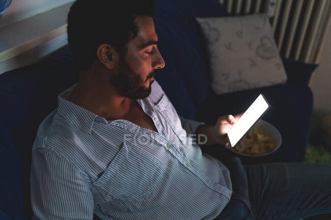 Чоловік дивиться на освітлений телефон у темній кімнаті — стокове фото