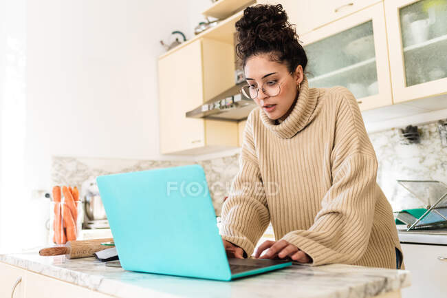 Jovem mulher usando laptop na cozinha — Fotografia de Stock