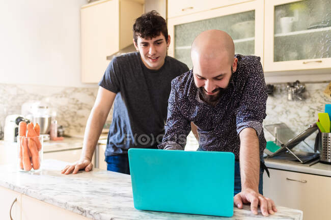 Молоді чоловіки дивляться на ноутбук на кухні — стокове фото