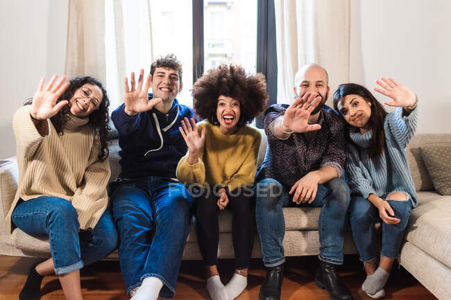 Friends sitting on sofa, waving on video call — Stock Photo