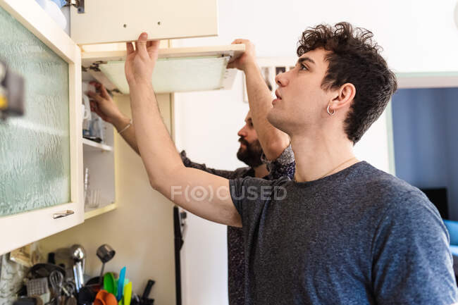 Jeunes hommes regardant dans les armoires de cuisine — Photo de stock