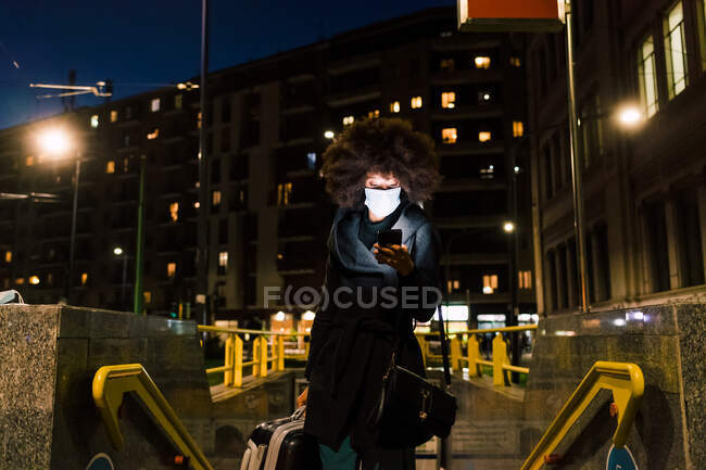 Mujer con mascarilla, mirando el teléfono, viajando por la noche - foto de stock