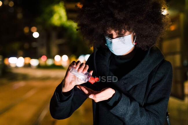Jeune femme portant un masque facial, appliquant un désinfectant pour les mains, à l'extérieur — Photo de stock