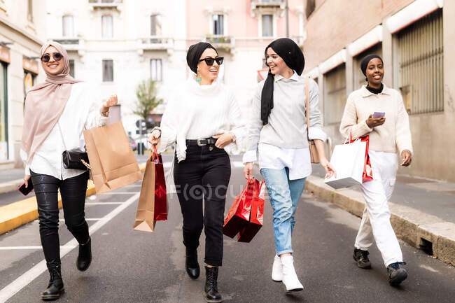 Quatre amies marchant le long de la rue avec des sacs à provisions — Photo de stock