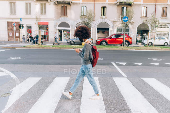 Young walking across road, looking at phone — Stock Photo