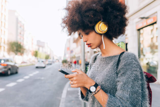 Молода жінка дивиться на телефон на відкритому повітрі, носить навушники — стокове фото