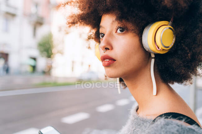 Jovem mulher usando fones de ouvido, olhando para o lado, ao ar livre — Fotografia de Stock
