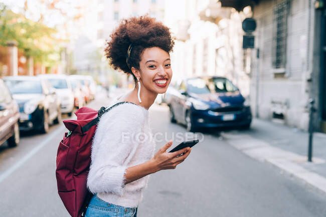 Young woman in street holding phone and smiling — Stock Photo