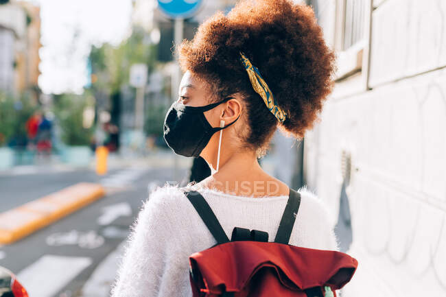 Young woman walking in city, wearing face mask, rear view — Stock Photo