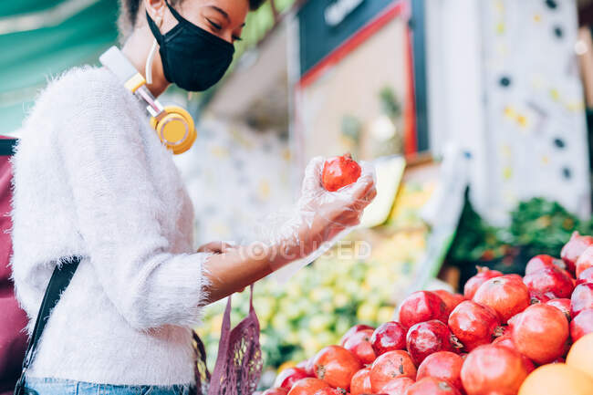 Молода жінка, яка вибирає фрукти за столом, носить маску для обличчя та рукавички — стокове фото