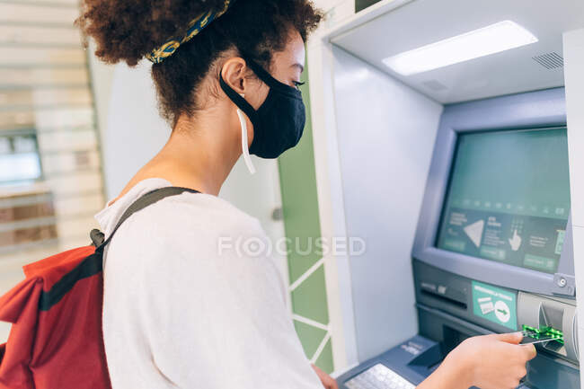 Jeune femme portant un masque facial, en utilisant ATM — Photo de stock