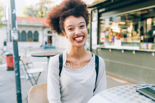 Молода жінка сидить за столом у кафе, усміхаючись. — стокове фото