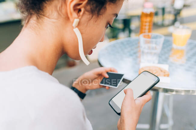 Young woman using phone and credit card at outdoor cafe — Stock Photo