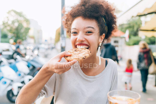 Jeune femme mangeant des biscuits au café extérieur — Photo de stock