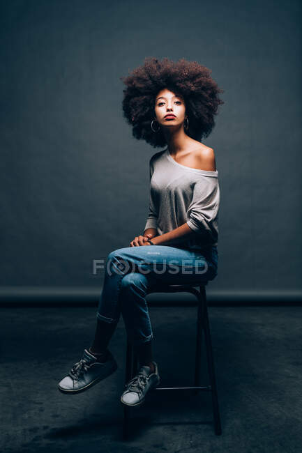 Portrait of a young woman sitting on stool — Stock Photo