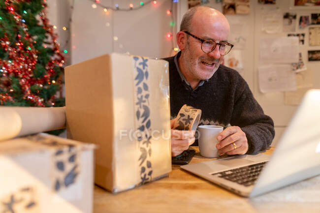 Человек упаковывает посылки и использует ноутбук — стоковое фото