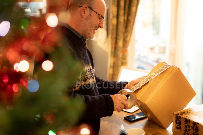 Мужчина упаковывает посылки на Рождество дома — стоковое фото