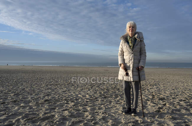 Старша жінка стоїть на пляжі і дивиться на камеру. — стокове фото