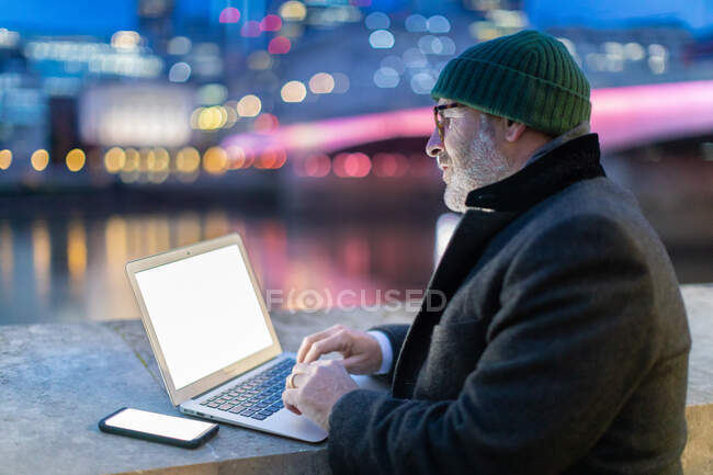 Man working on laptop in city at night, London, UK — Stock Photo