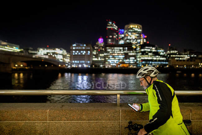 Ciclista con teléfono en la ciudad por la noche, Londres, Reino Unido - foto de stock