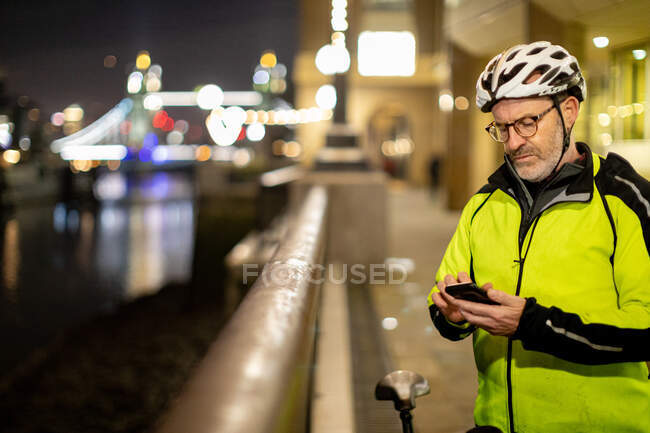Ciclista usando el teléfono en la ciudad por la noche, Londres, Reino Unido - foto de stock