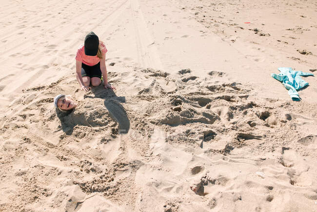 Girl burying brother in sand on beach — Stock Photo