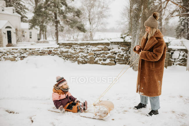 Canada, Ontario, Mother pulling daughter (2-3) on toboggan — Stock Photo