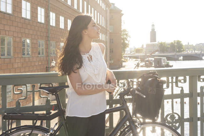Schweden, Stockholms Lan, Stockholm, Junge Frau mit Fahrrad steht auf Brücke — Stockfoto