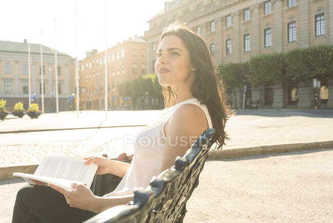 Schweden, Stockholms Lan, Stockholm, Junge Frau sitzt auf Bank und hält Buch — Stockfoto