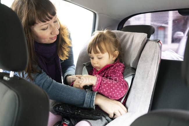Madre poniendo hija en el asiento del coche - foto de stock