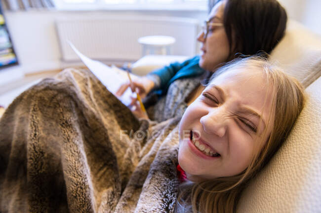 Великобритания, Суррей, мать и улыбающаяся дочь (10-11 лет) на диване дома — стоковое фото