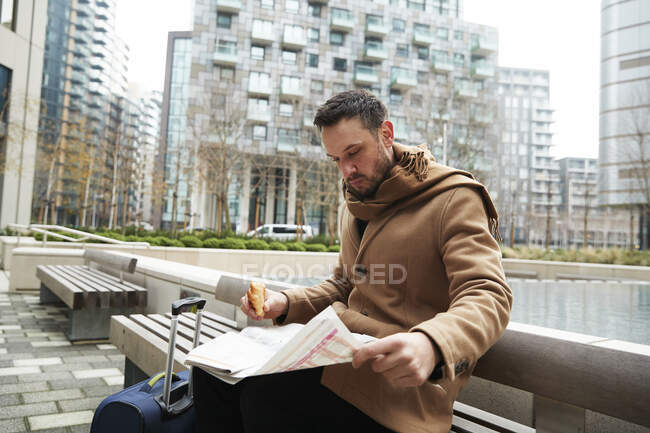 Великобритания, Лондон, Мужчина читает газету на скамейке — стоковое фото