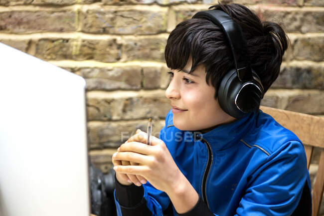 Reino Unido, Sonriente niño (10-11) en los auriculares que tienen lección en línea - foto de stock