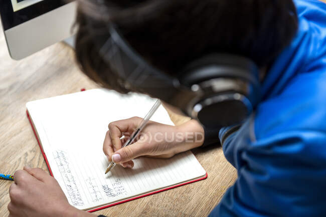 Великобритания, мальчик (10-11 лет) в наушниках, пишет в тетрадке — стоковое фото