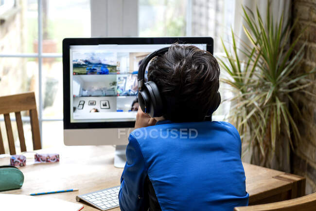 Reino Unido, Vista trasera del niño (10-11) con auriculares sentados delante de la computadora - foto de stock