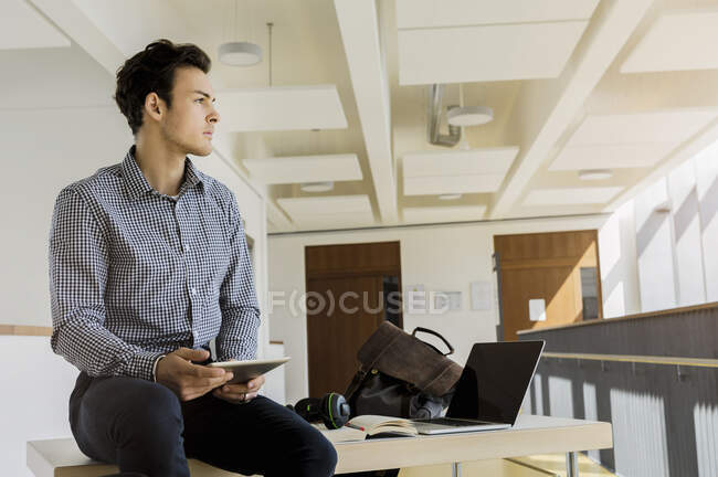 Germany, Bavaria, Munich, Young man sitting on desk with digital tablet — Stock Photo