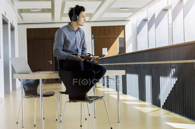 Germany, Bavaria, Munich, Young man with headphones sitting on desk — Stock Photo