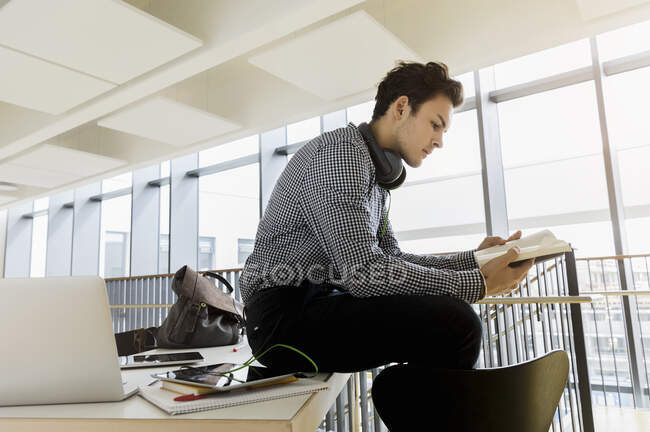 Allemagne, Bavière, Munich, Jeune homme assis sur le bureau et le livre de lecture — Photo de stock