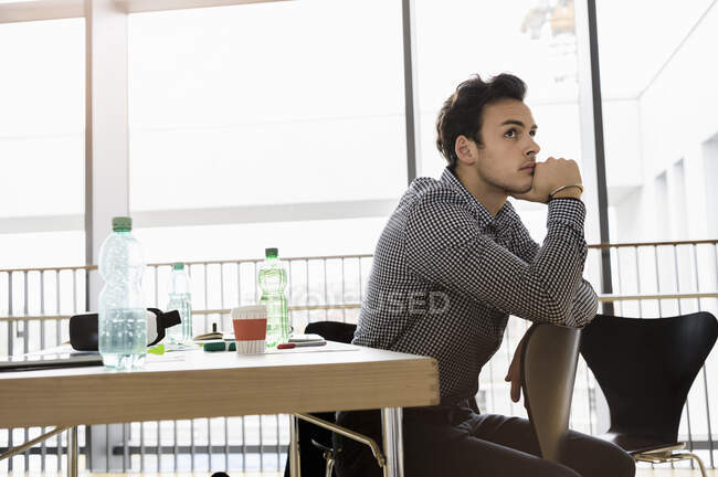 Allemagne, Bavière, Munich, Jeune homme assis sur une chaise par bureau et réfléchissant — Photo de stock