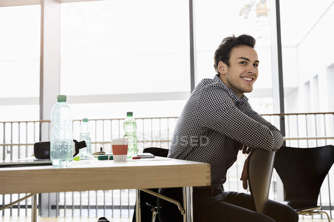 Allemagne, Bavière, Munich, Jeune homme assis sur une chaise par bureau et souriant — Photo de stock