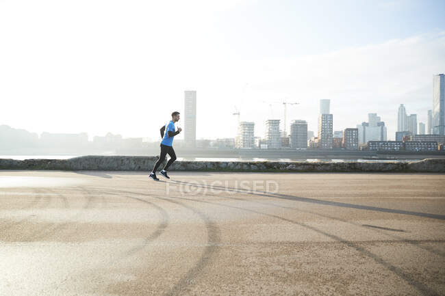 Reino Unido, Londres, Jogger corriendo con horizonte del centro de la ciudad en segundo plano - foto de stock