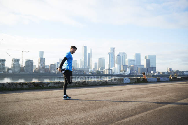 UK, London, Jogger stretching with downtown skyline in background — Stock Photo