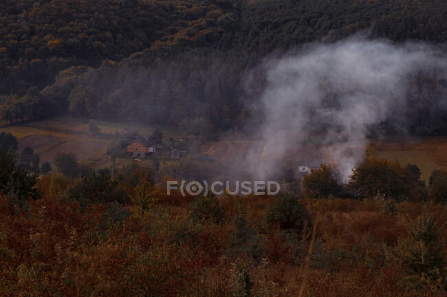 Ucrania, Humo saliendo de las casas de pueblo en el paisaje de otoño - foto de stock