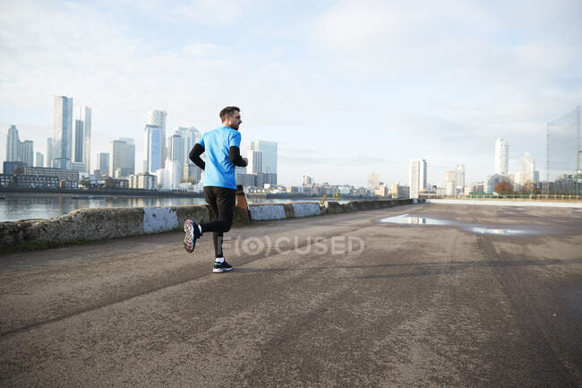 Reino Unido, Londres, Jogger corriendo con horizonte del centro de la ciudad en segundo plano - foto de stock