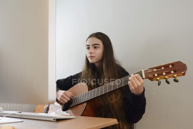 Mädchen spielt Gitarre vor dem Computer — Stockfoto