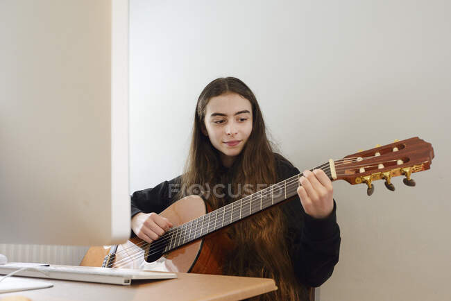 Girl playing guitar in front of computer — Stock Photo