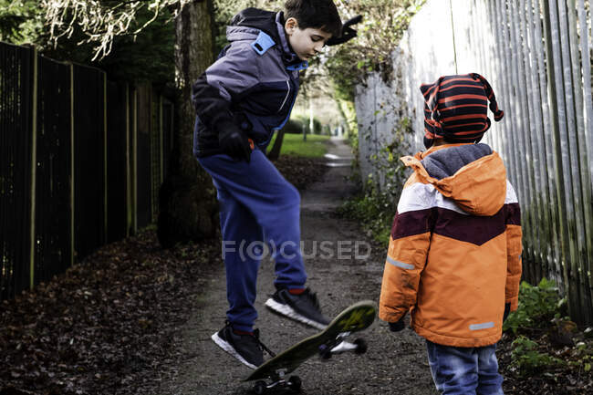 Reino Unido, Two boys (4-5, 10-11) playing with skateboard - foto de stock